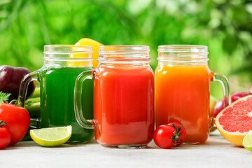 Mason jars with healthy juice, fruits and vegetables on table outdoors, closeup