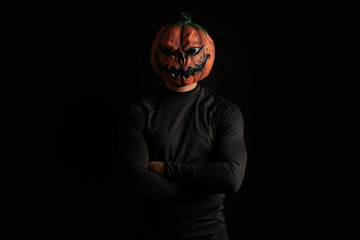 Man wearing Halloween pumpkin mask, arms crossed, in front of a black background.
