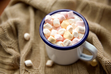 season, leisure and objects concept - camp mug full of marshmallow on knitted blanket