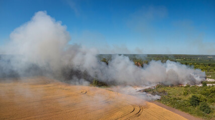 Burning garbage site near agricultural field in the countryside. Dangerous fire near agricultural field