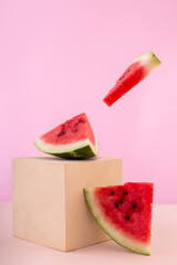 Ripe watermelon slices on beige cube podium on pink background. Vertical image with food levitation and modern pastel pedestal. Flying piece of red watermelon