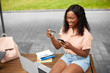 technology, education and people concept - happy smiling african american student girl with smartphone and credit card in city