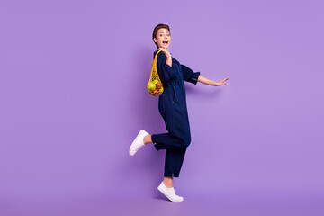 Full size profile side photo of young excited smiling girl go walk shopping reusable net bag isolated on violet color background