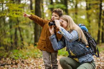Happy mother and son are hiking in forest. They are watching nature with binoculars.