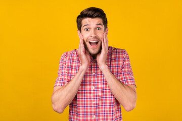 Photo of amazed shocked young happy man hold hands cheeks news sale isolated on yellow color background