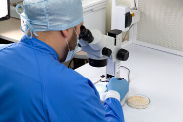 A male scientist in a mask looks through a microscope in a laboratory.