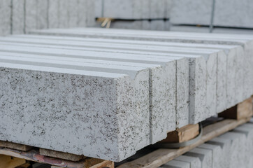 Close-up of gray curbs stacked on pallets. New concrete curbs taped together. Repair and construction work. Outside. Selective focus. No people.