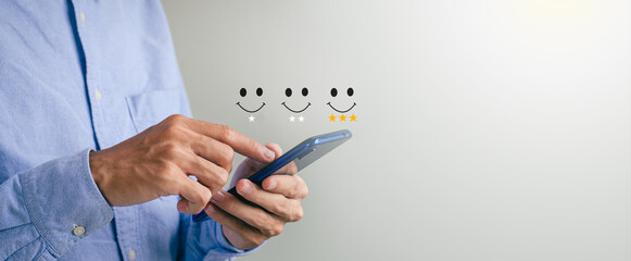 Customer Satisfaction Rating Concept A man holds a smartphone watching a performance on a scoring screen with a three-star gold symbol and a smiling face to her satisfaction. - obrazy, fototapety, plakaty
