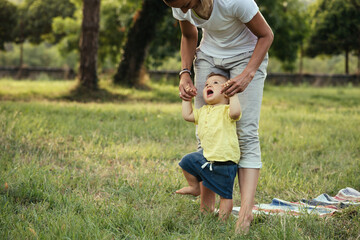 mother and her baby boy playing outdoor in public park. learning to walk