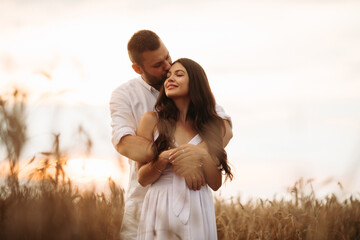 Pretty caucasian woman with long dark wavy hair in white dress hugs with beautiful man in white t-shirt and shorts