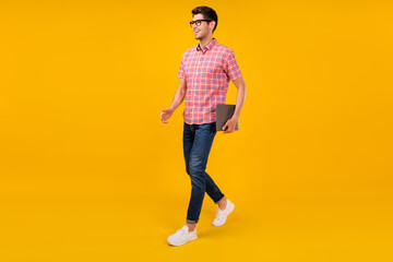 Full length body size view of attractive cheerful guy going holding laptop isolated over bright yellow color background