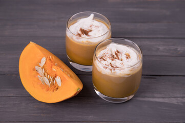 Two glasses of pumpkin latte with sliced pumpkin on a dark background. Autumn drink