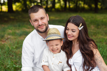 Picture of cheerful young caucasian female and male holds their child on hands, smiles and rejoices