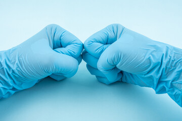 Hands wearing blue disposable gloves clenched fists