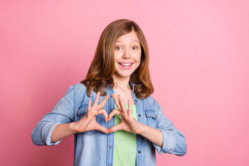 Photo portrait girl smiling showing heart sign with fingers dreamy happy isolated pastel pink color background