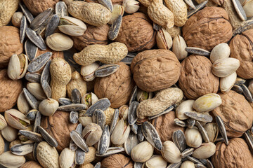 Heap of mixed nuts as background: walnut, peanut, pistachio and sunflower seed. Top view