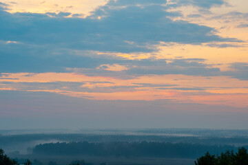 A slightly hazy landscape with steam rising between the trees. Evaporation in the forest on sunset after rain.