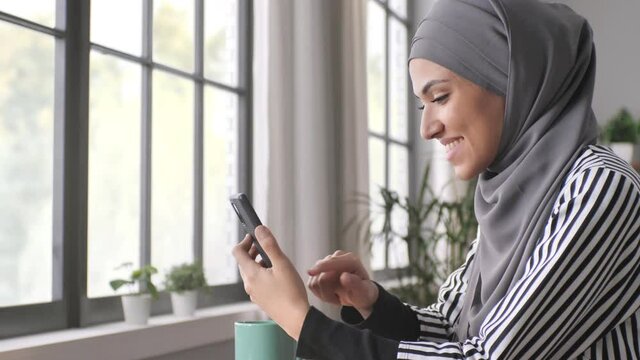 arab young woman in hijab using smart phone mobile at the cafe,connected muslim girl sits at the table holding smartphone browsing internet social media network 