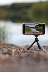 A close up of the phone on a tripod takes a video or a photo of nature. A beautiful lake in the...