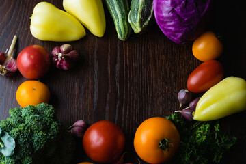 Concept of vegetarianism and proper nutrition. Vegetables tomatoes, garlic, zucchini, cabbage, cilantro, peppers on a dark wooden table top, top view, copy space in the center.