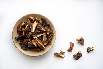 Small pieces of boletus edulis in a bowl and isolated on white background. Dried organic mushrooms, healthy diet. Selective focus on the details, blurred background.