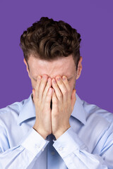 Young man closing eyes with hands isolated on purple color studio background. Concept of human emotion, facial expressions, youth, feelings, ad.