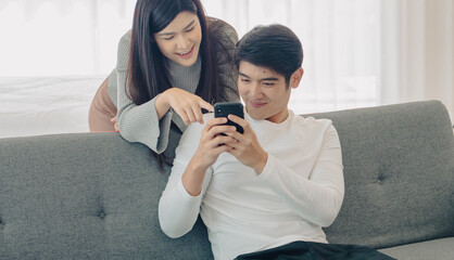 Young couple stay home together remote connected with friends using smartphone and internet wireless technology. Happy handsome man and girlfriend smiling chatting online. Husband and wife talking.