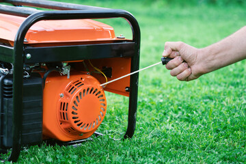 Hand starts a portable gasoline electric generator standing on the green grass