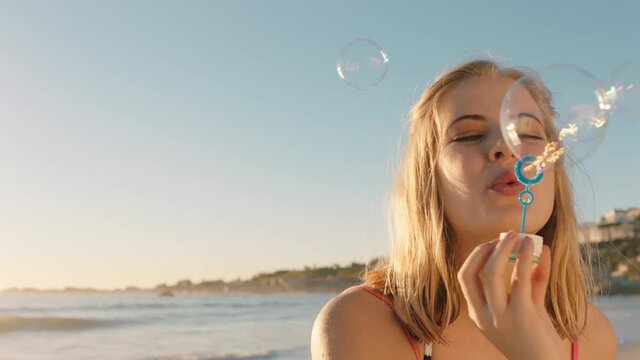 beautiful woman blowing bubbles on beach at sunset enjoying summer having fun on vacation by the sea