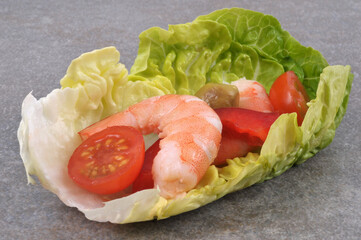 Amuse-bouche avec une feuille de salade, une crevette, une oilve verte et une tomate en gros plan sur fond gris