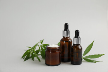 Cream, hemp leaves, bottles of CBD oil and THC tincture on light grey background. Space for text