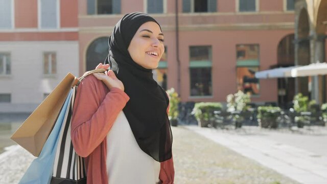 happy muslim young arab woman in hijab walking holding shopping bags city background,pleased arab girl walks down the historic center,she is satisfied of her purchases