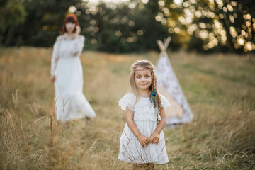 Pretty little blond child girl in white dress and with feather in the hair, posing at camera...