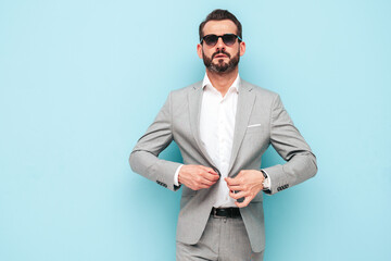 Portrait of handsome confident stylish hipster lambersexual model.Modern man dressed in elegant suit. Fashion male posing in studio near blue wall in sunglasses