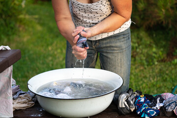 Woman wrings out underwear to an old basin outdoors in summer