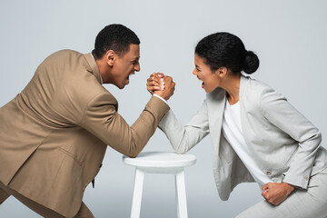 side view of african american businesswoman and man doing arm wrestling on white chair isolated on...