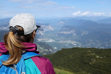 Fototapeta na wymiar The girl standing backwards with the backpack looks at the Adige valley from the Paganella peak in Trentino.