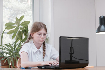Schoolgirl self isolation using laptop for his homework. Girl doing using digital tablet searching...