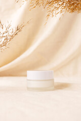 Cream beauty product mockup on linen drapery and dry branch of meadow plant. Concept eco organic...