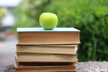 Stack of hardcover books and green apple in a garden. Selective focus. Back to school concept.