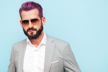 Portrait of handsome confident stylish hipster lambersexual model.Modern man dressed in elegant suit. Fashion male posing in studio near blue wall in sunglasses. WIth pink hair