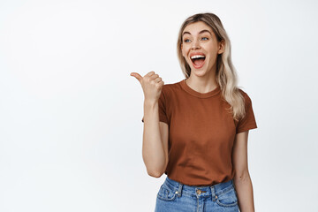 Fototapeta na wymiar Portrait of young candid woman laughing, pointing and looking left at smth funny, standing in tshirt and jeans against white background