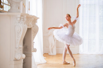 young slender ballerina in a white tutu in pointe shoes is dancing in large beautiful white hall.