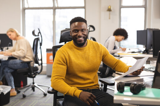 Portrait of smiling african american male creative at work, sitting at desk, looking to camera