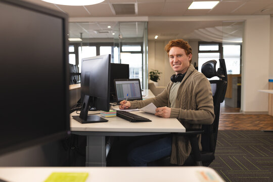 Portrait of smiling caucasian male creative at work, sitting at desk, looking to camera