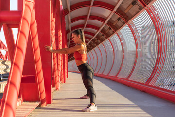 Chica estirando aductores, al aire libre en un puente rojo.