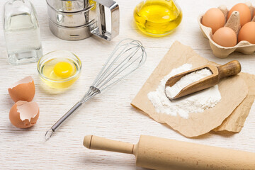 Rolling pin and whisk. Scoop with flour on paper. Chicken shells and eggs in container.