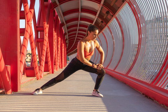 Chica estirando aductores en aire libre, en un puente rojo.