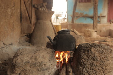 horizontal closeup photography of an old black kettle, standing over yellow and orange fire flames, on three stones, outdoor on a sunny day in the gambia, Africa - obrazy, fototapety, plakaty