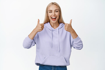 Fototapeta na wymiar Happy blond girl laughing and showing thumbs up, approving something, agree and like company, standing over white background
